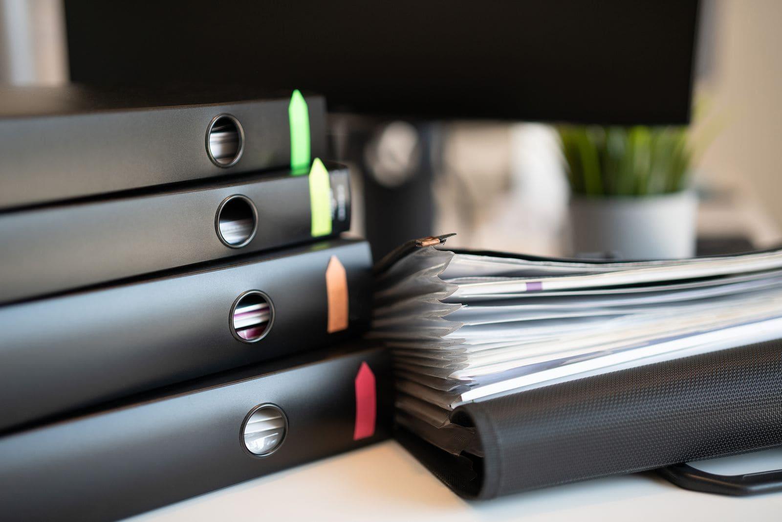 A stack of ring binders and a full document wallet on a desk