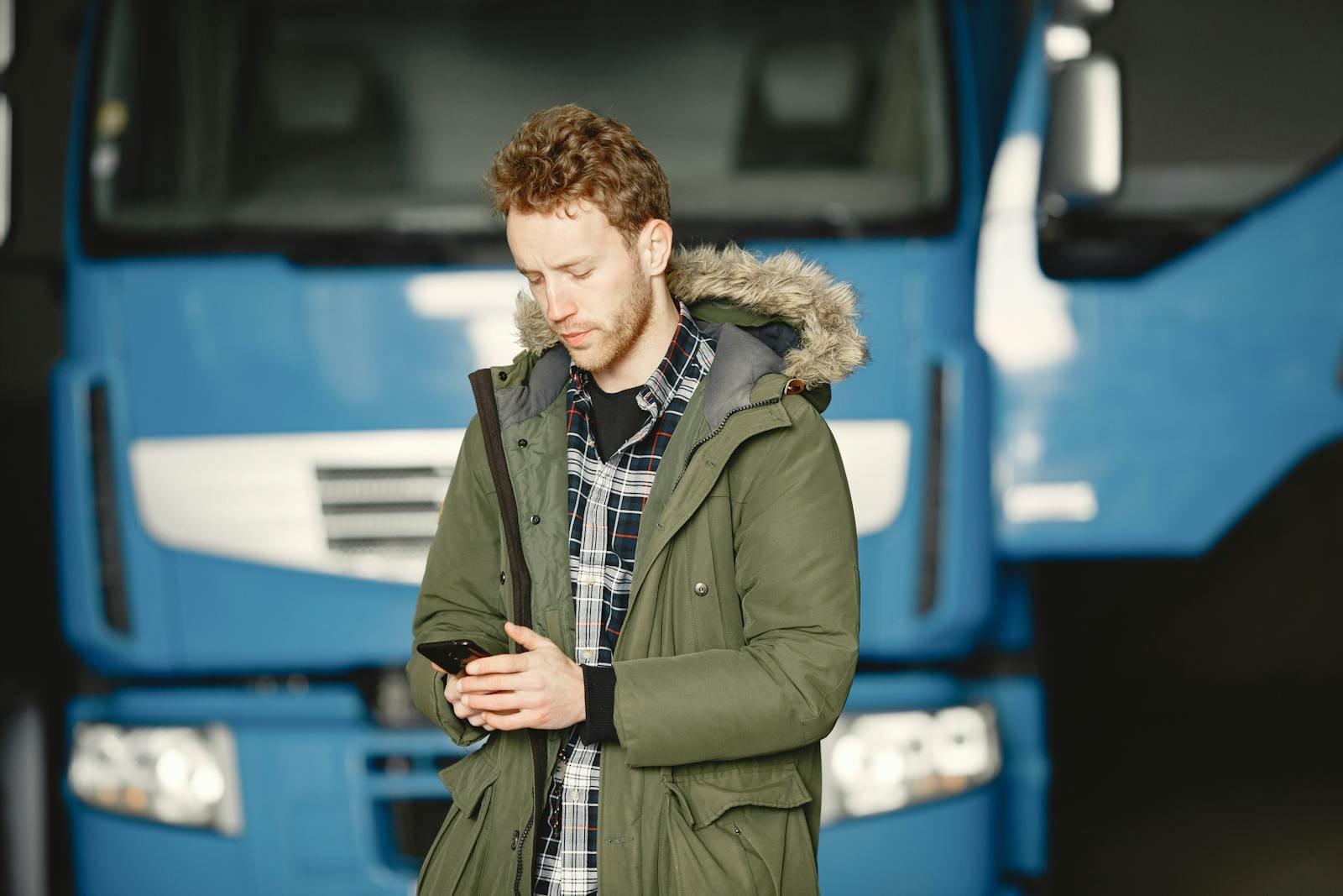 A man in a parka checking his phone, standing in front of parked trucks