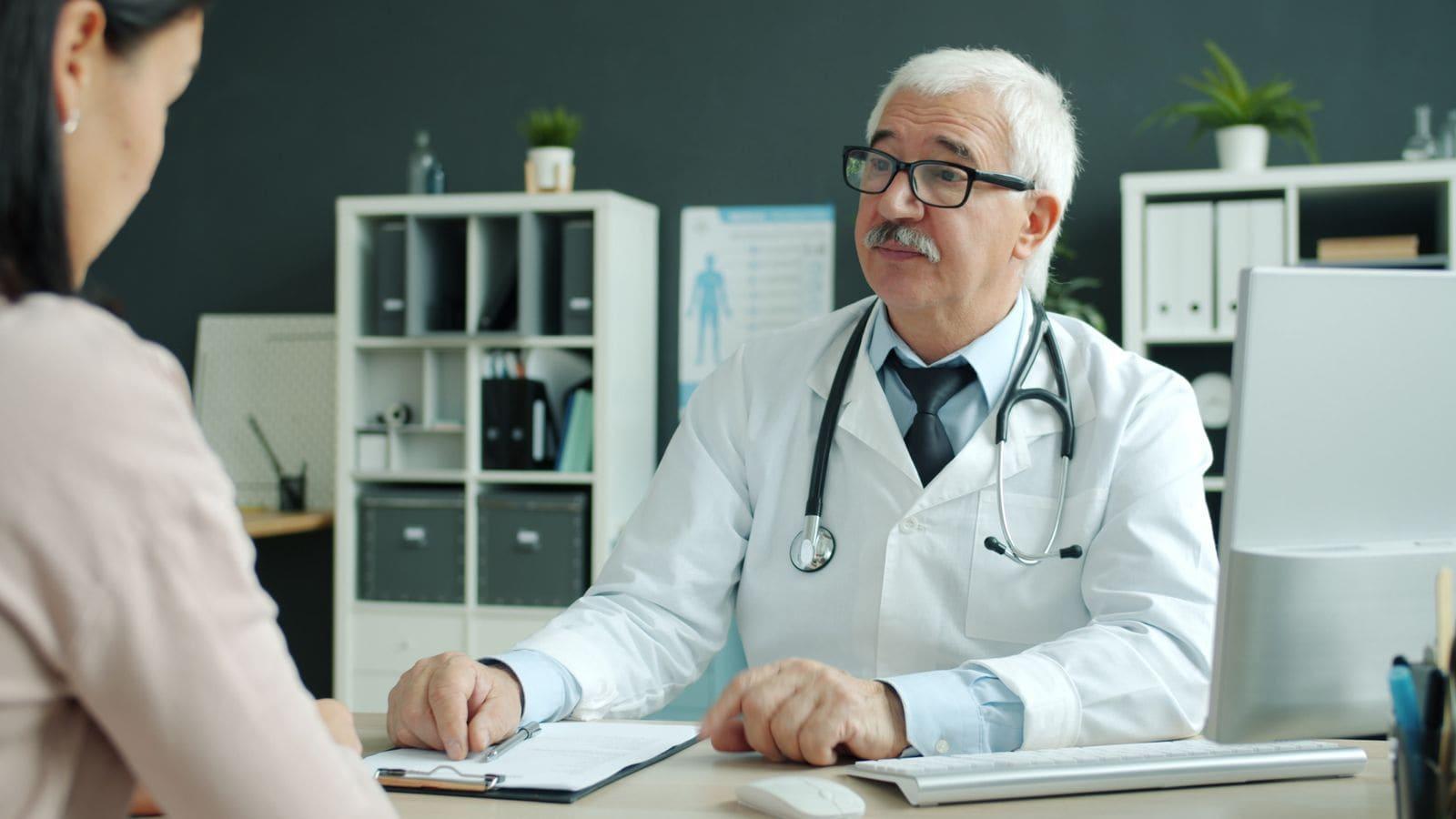 A doctor listening to a patient across the desk in a bright consulting room